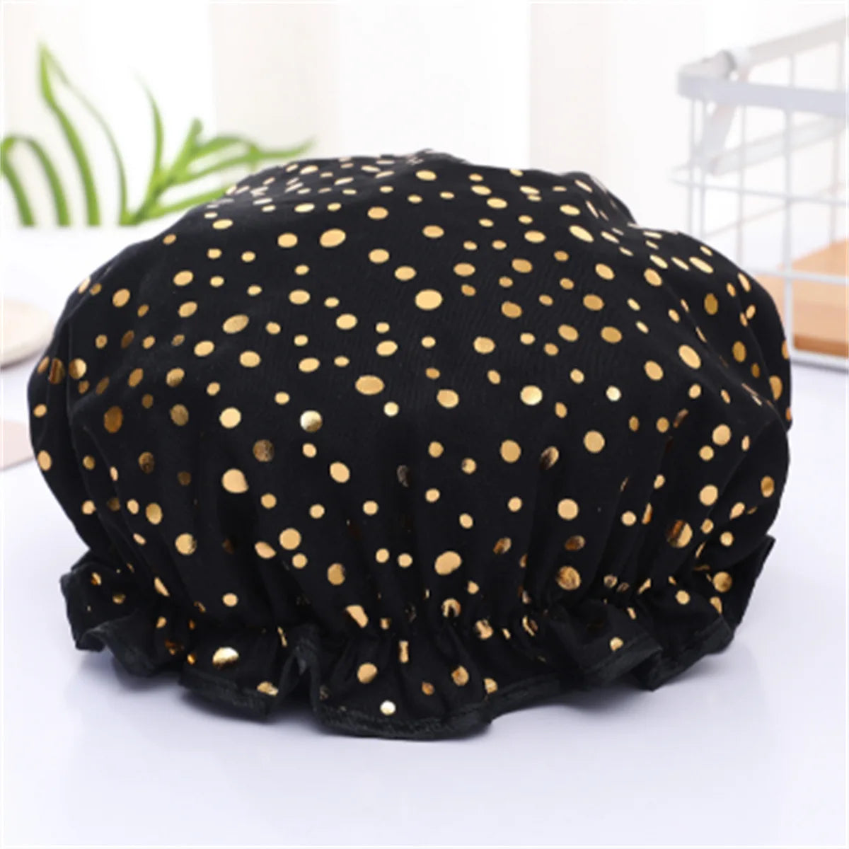 Black elastic shower cap with gold polka dots shown on a white surface.