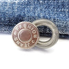 Silver extender buttons with a round charm featuring the word FASHION and jeans symbols, placed on denim fabric.