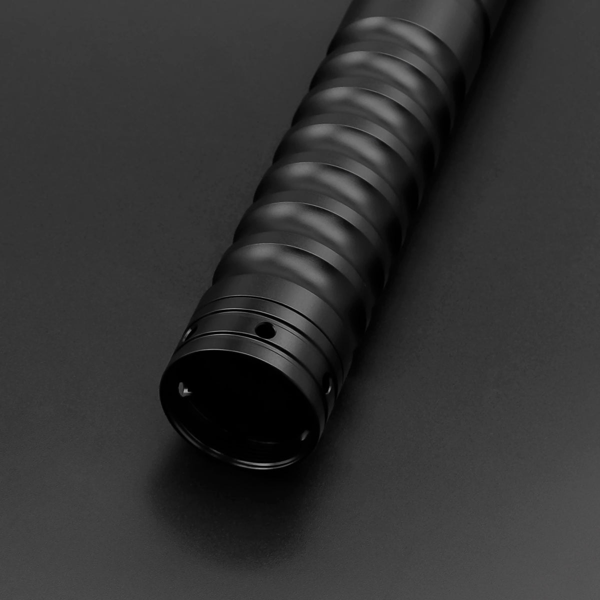 A close-up view of a black metal lightsaber hilt with ribbed texture.