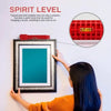 A hand is hanging a framed picture on a wall, demonstrating the use of a spirit level.