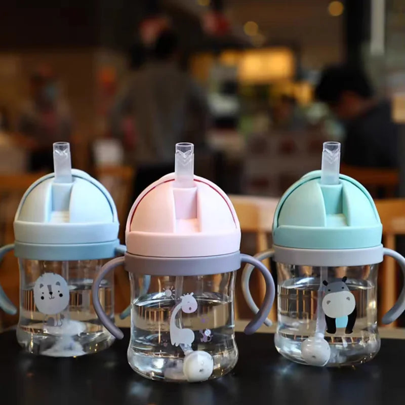 A set of clear plastic straw cups with handles in pastel colors pink and mint green sitting on a dark surface.