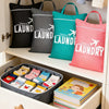 A set of black, gray, and teal fabric laundry bags hanging in a closet, with a storage box full of folded laundry nearby.
