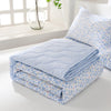 Light blue and white quilted blanket folded on a white surface next to a window.