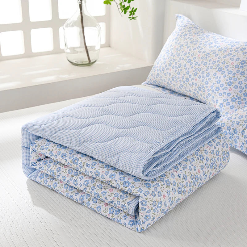 Light blue and white quilted blanket folded on a white surface next to a window.