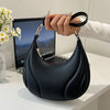 A hand holds a black textured crossbody bag with a gold chain strap against a white background.