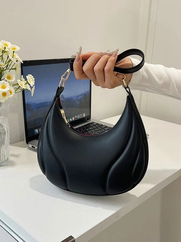 A hand holds a black textured crossbody bag with a gold chain strap against a white background.