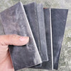 Two pieces of black buffalo horn knife handle scales are shown angled against a gray background.