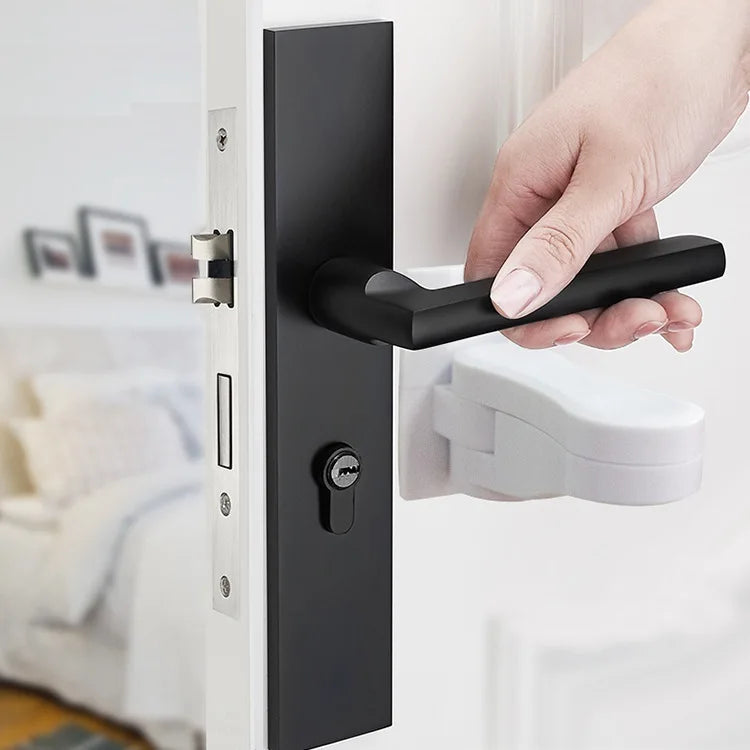 A hand is operating a black door lever lock on a white door, demonstrating an adhesive anti-open latch for handles.