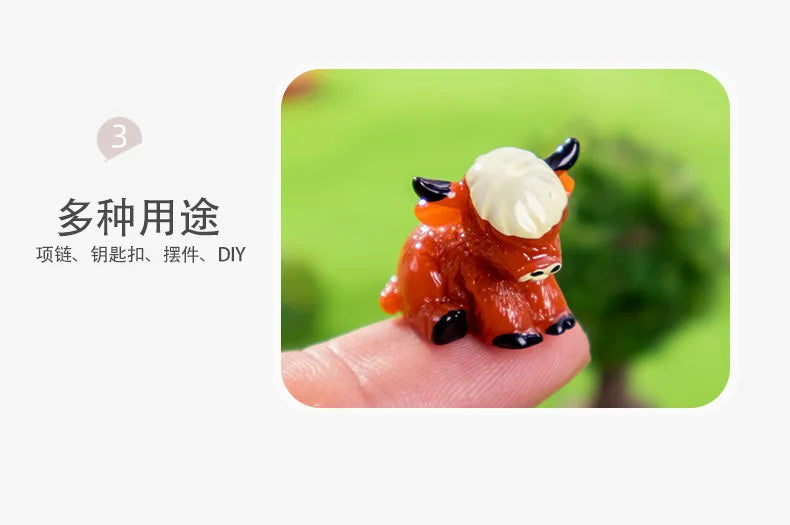 An adorable orange resin Highland cow figurine resting on a person's finger against a blurred green background.