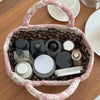 A pink quilted fabric storage basket filled with various small glass and plastic containers for organizing home or desk items