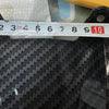 A close-up view of a black carbon fiber rear fender mudguard being measured with a ruler.