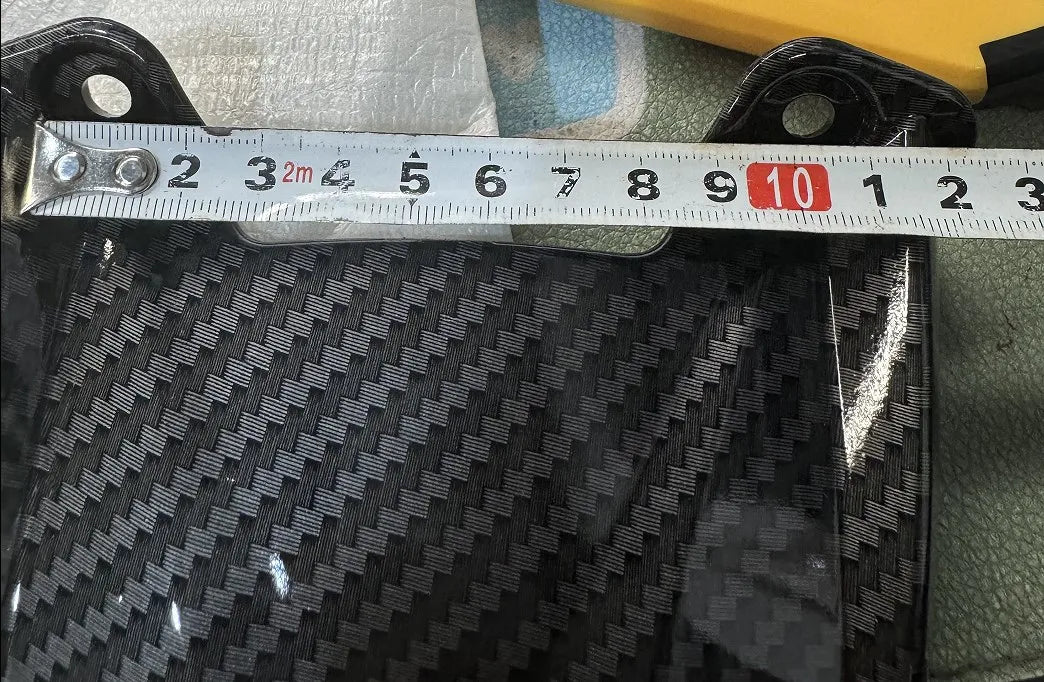 A close-up view of a black carbon fiber rear fender mudguard being measured with a ruler.