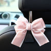 A pink bow-shaped car seat back hook with storage attached to a black car seat.