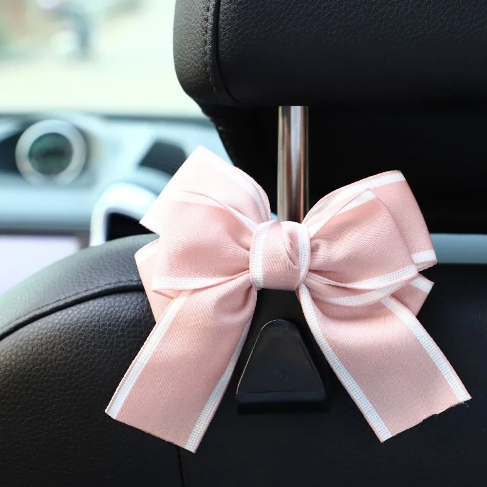 A pink bow-shaped car seat back hook with storage attached to a black car seat.