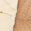 A gold-tipped quilting pin is shown resting on a light cream fabric next to a wooden surface.