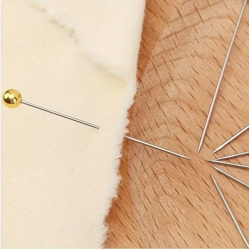 A gold-tipped quilting pin is shown resting on a light cream fabric next to a wooden surface.