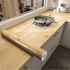 A roll of self-adhesive wood grain waterproof wallpaper is displayed on a light wooden countertop.
