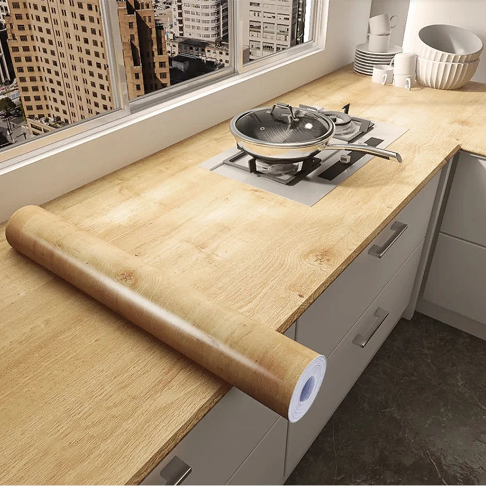 A roll of self-adhesive wood grain waterproof wallpaper is displayed on a light wooden countertop.