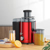 A red and black centrifugal juicer appliance with a stainless steel feed tube and a glass juice container on a wooden surface