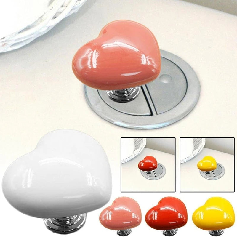 Heart-shaped toilet flush button in pink, white, and yellow colors with a silver base.