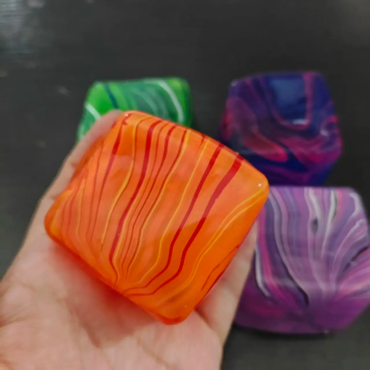Une main tient un cube de jeu en gel apaisant orange et ondulé, à côté d'autres cubes colorés.