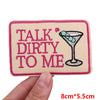 Pink embroidered patch with text 'TALK DIRTY TO ME' and a cocktail icon on a beige fabric background