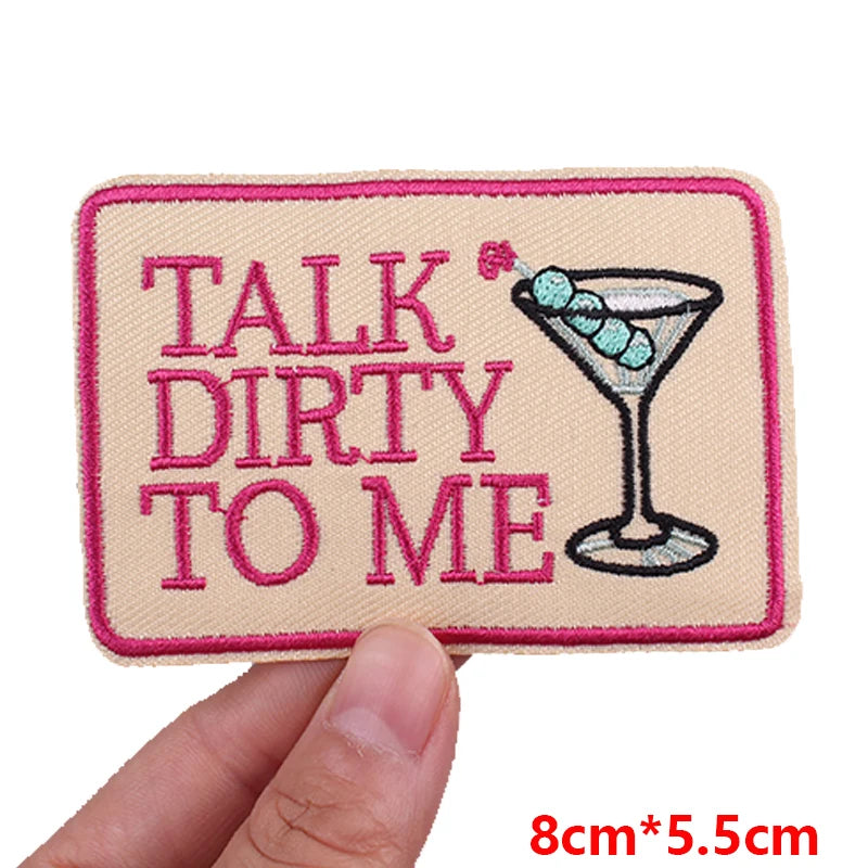 Pink embroidered patch with text 'TALK DIRTY TO ME' and a cocktail icon on a beige fabric background