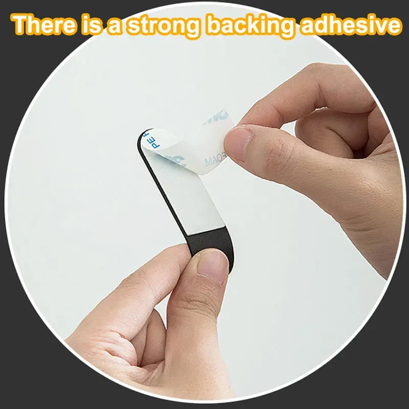 A hand is applying a piece of white adhesive tape to a black hook, demonstrating strong backing adhesive.