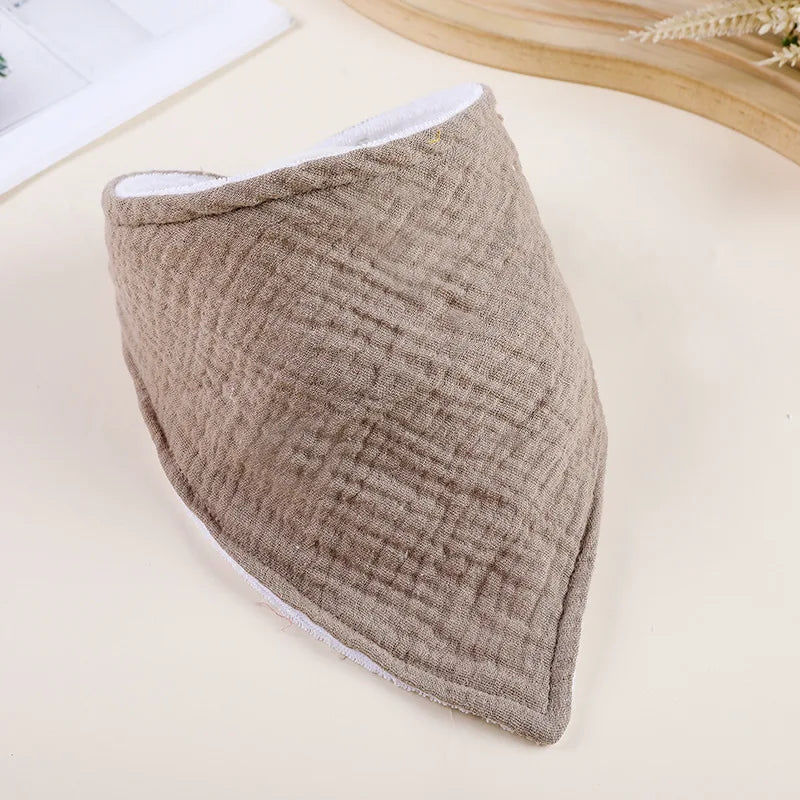 A beige ribbed soft cotton baby bib is shown on a light surface.