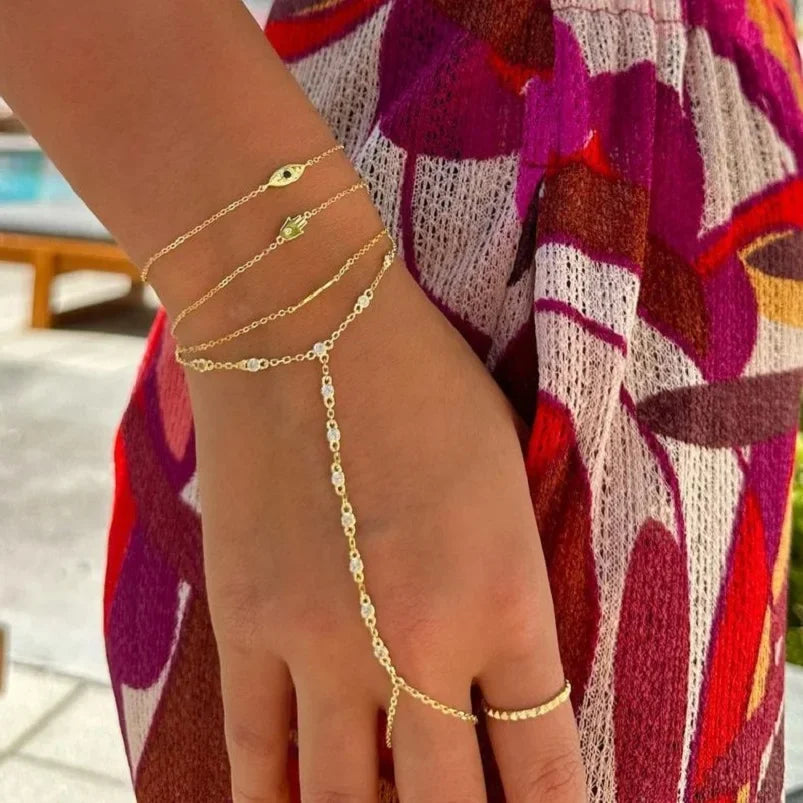 A hand wearing a gold CZ link chain bracelet against a purple and red patterned fabric.