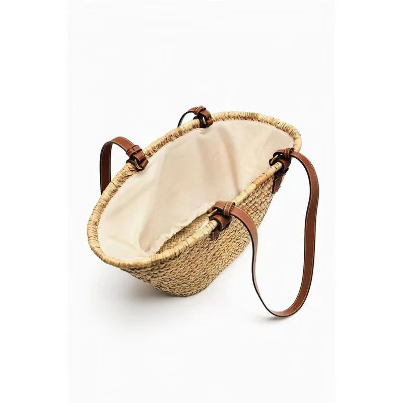 A handwoven straw tote bag with a light beige lining and brown leather straps.