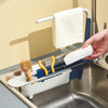 A hand is holding a white sponge hanging from an adjustable sink holder with a drainer basket.