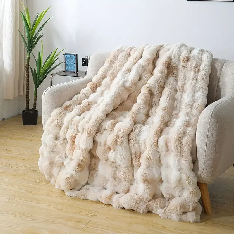 Flauschiges beige Kunstfahreins blanket über einem hellen Sofa.