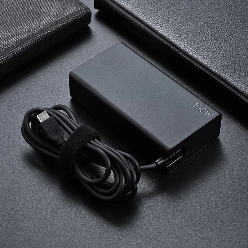 Schwarzer 100W USB-C PD Laptop-Ladegerät und Kabel auf dunkler Oberfläche.