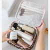 A hand opens a leopard print toiletry bag with a pink lining, revealing various skincare products inside.