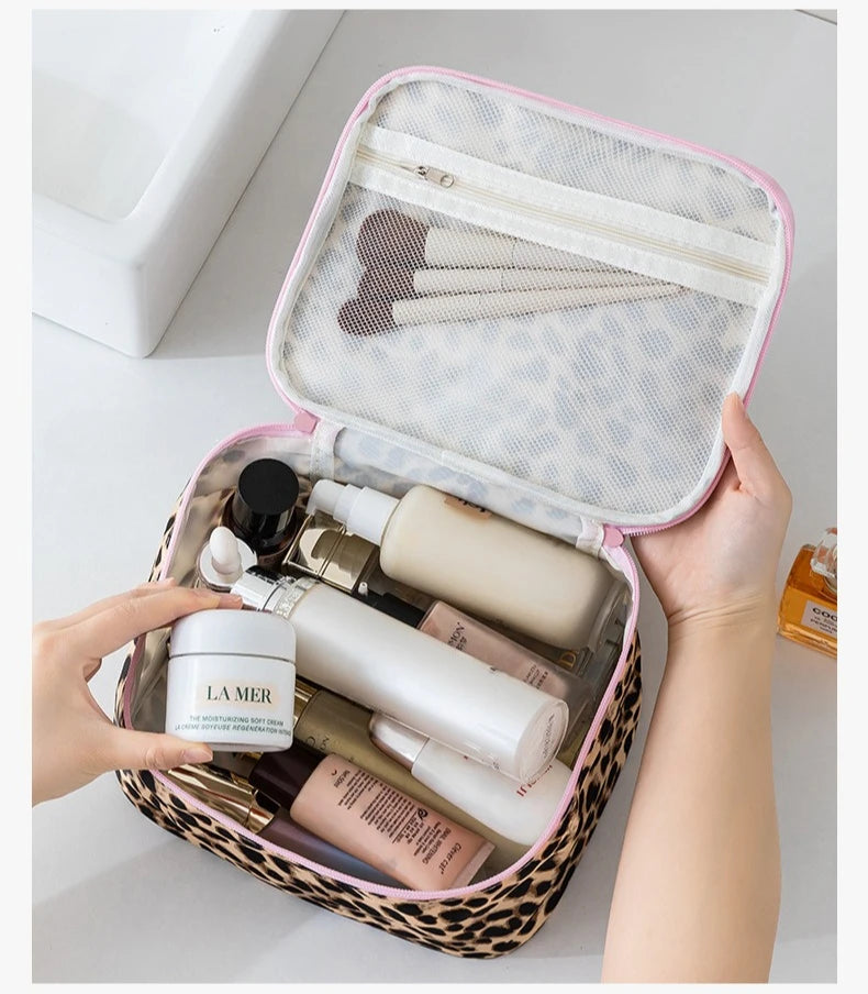 A hand opens a leopard print toiletry bag with a pink lining, revealing various skincare products inside.