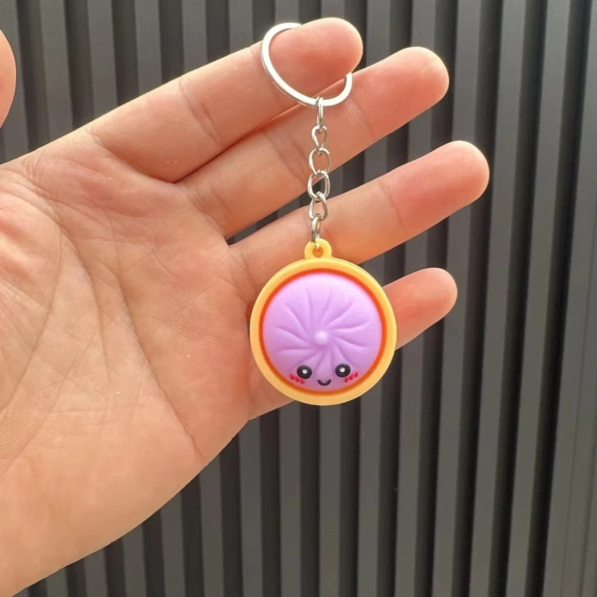 Eine Hand hält einen dekorativen Dumpling-Anhänger mit lila und gelbem Design.