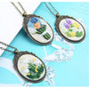 A set of three floral embroidery necklaces with silver chains and oval fabric patterns on a light blue background.