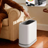 A white touchless trash can is shown on a wooden floor, with a hand opening the lid and an inset showing color options.