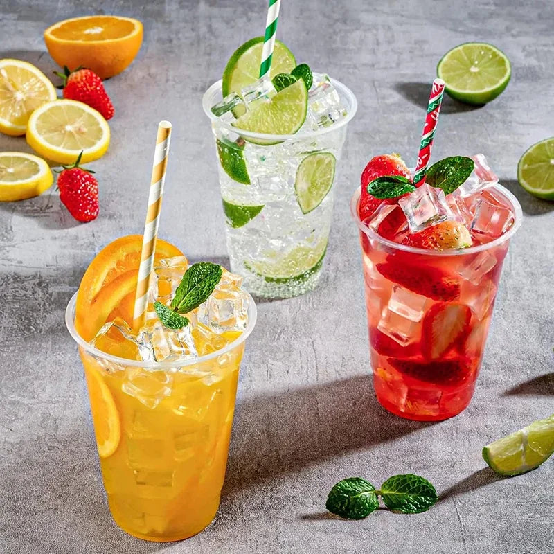 A collection of colorful iced drinks in clear plastic cups with straws and garnishes on a gray surface.