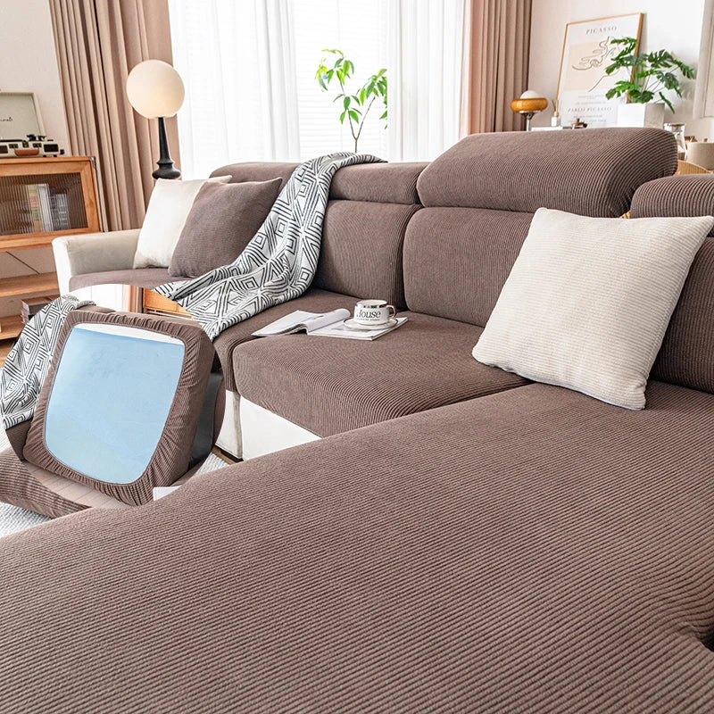 Sofá moderno color topo con cojines claros y una manta estampada en una sala de estar luminosa.