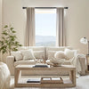 A living room scene featuring a light beige sofa, sheer curtains, and a wooden coffee table.