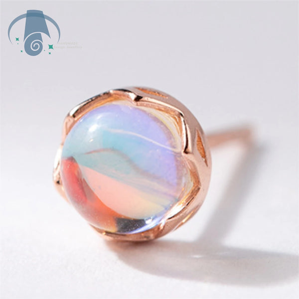 A close-up of minimalist moonstone stud earrings featuring a polished, iridescent gemstone.