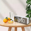 A digital clock displaying 12:30 is shown next to fresh oranges and a glass on a wooden table.