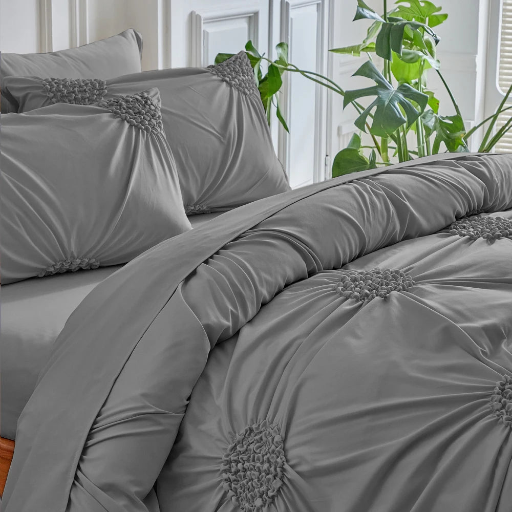 A gray three-dimensional pleated floral duvet cover set displayed on a bed with green foliage in the background.