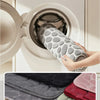 A hand is gently washing a gray, pebble-textured absorbent bathroom rug inside a white washing machine.