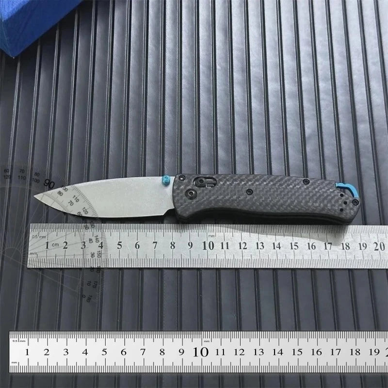 A carbon fiber folding knife with an axis lock is shown resting on a measuring ruler.