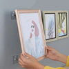 Hands holding a framed picture and two wooden frames with self-adhesive wall hooks.