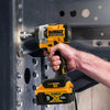 A hand holds a yellow and black DeWalt 20V XR brushless impact driver tool against a dark metal surface.