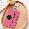 A pink leather card holder with a black spade charm and a metal keyring resting on a wooden board.